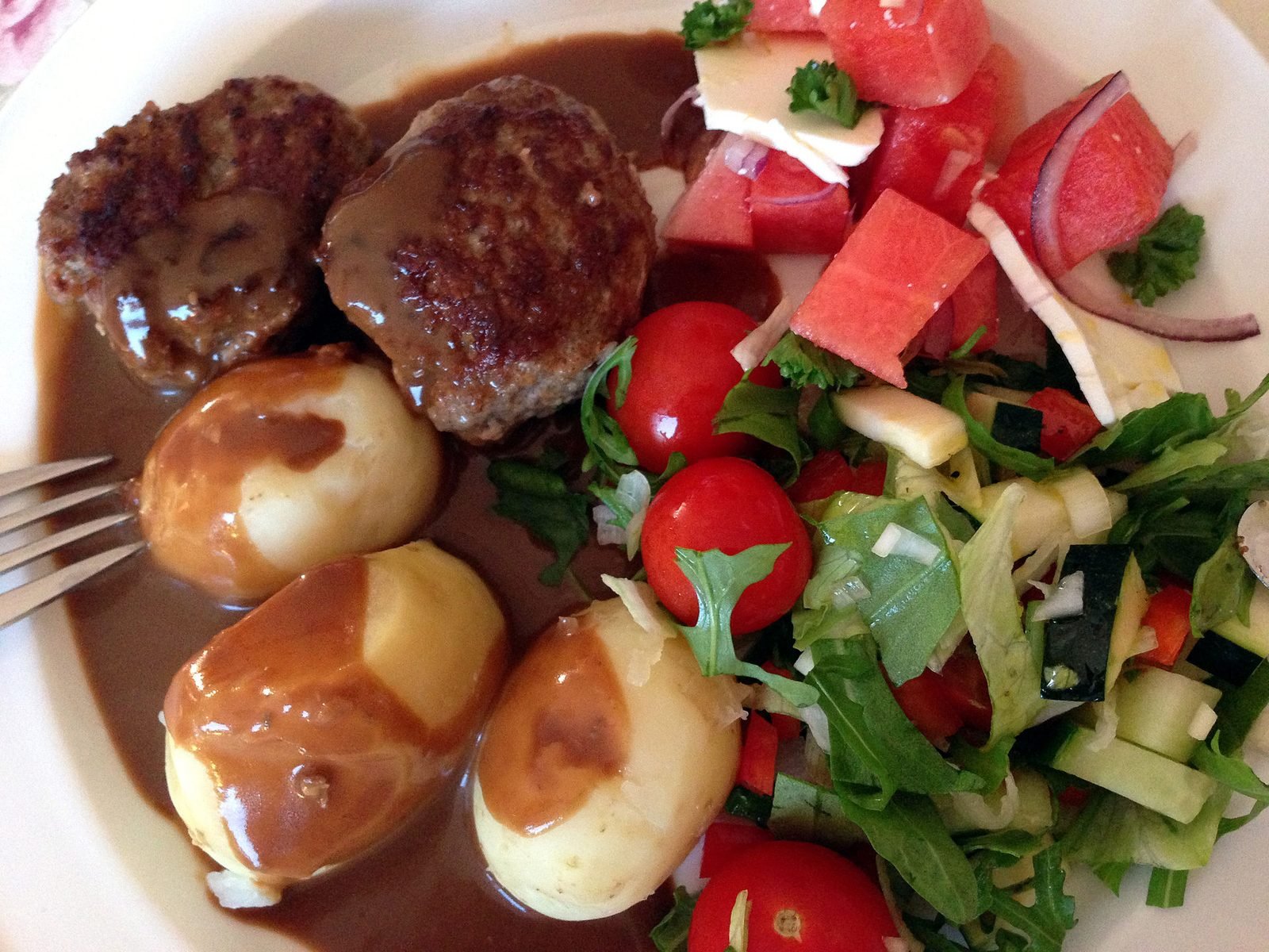 Frikadeller mit Kartoffeln, brauner Sauce und buntem Salat auf einem Teller
