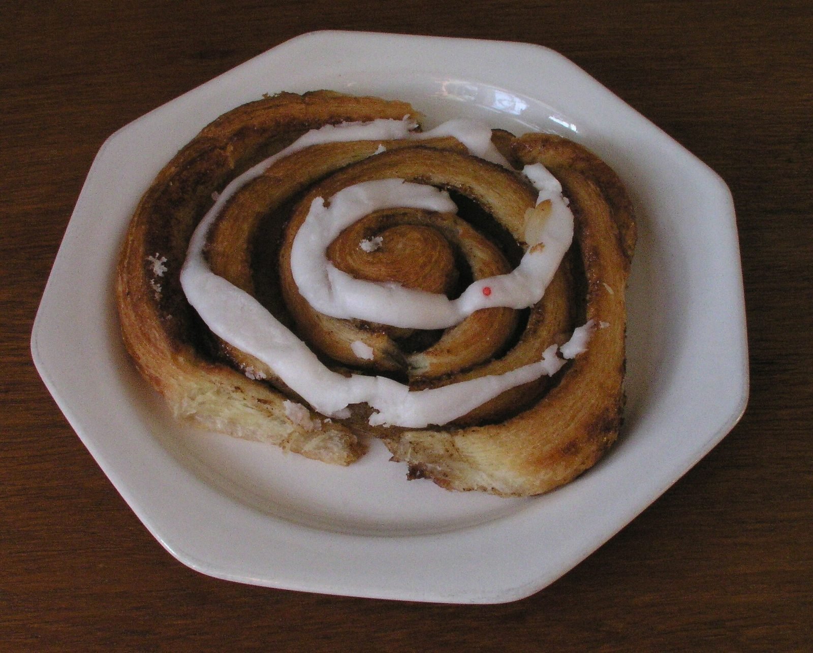 Dänische Zimtschnecke mit Zuckerguss auf einem weißen Teller